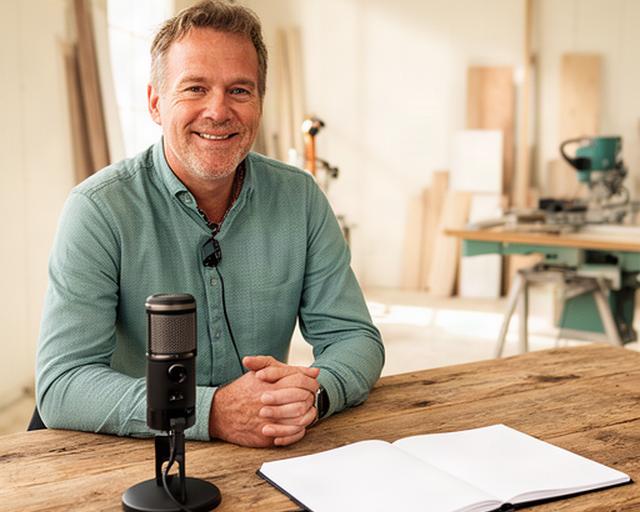 Gelderse ondernemer aan een houten tafel met podcastmicrofoon en notitieboek in een lichte bedrijfsruimte